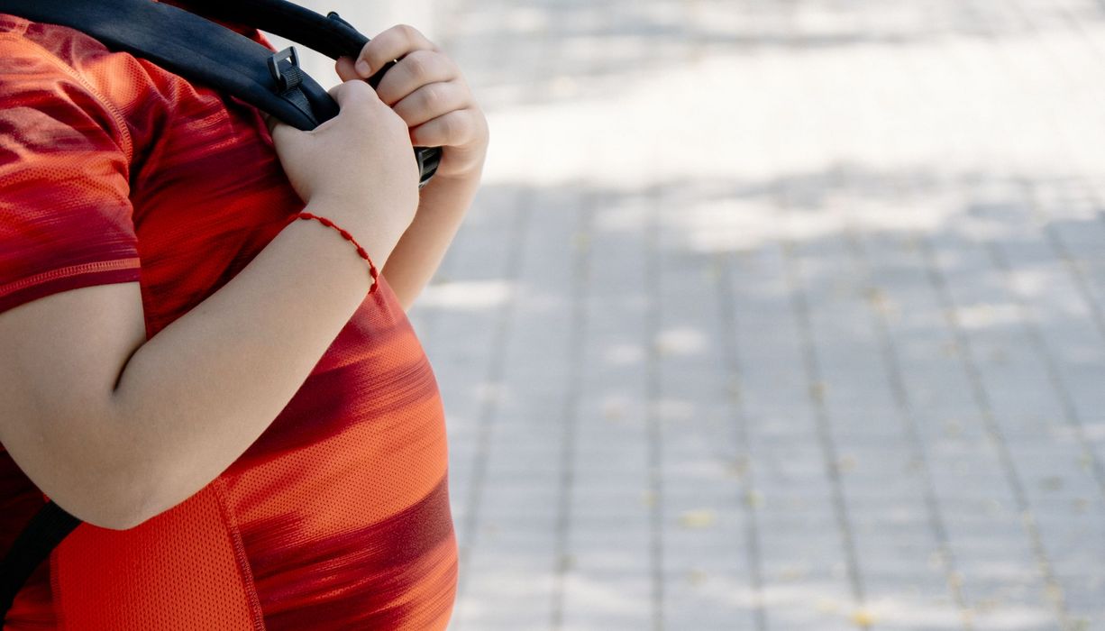 Profil von einem übergewichtigen Jungen mit Rucksack.