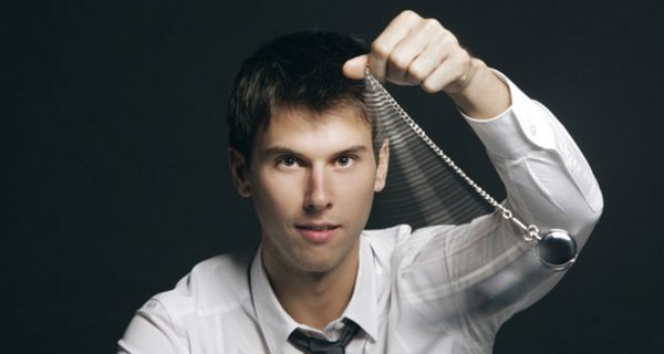 Mann in Hemd und Krawatte schwingt ein Pendel vor seinem Kopf