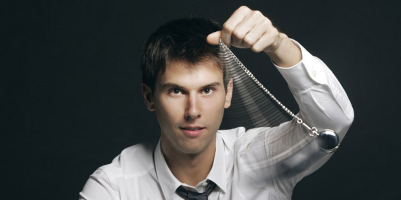 Mann in Hemd und Krawatte schwingt ein Pendel vor seinem Kopf