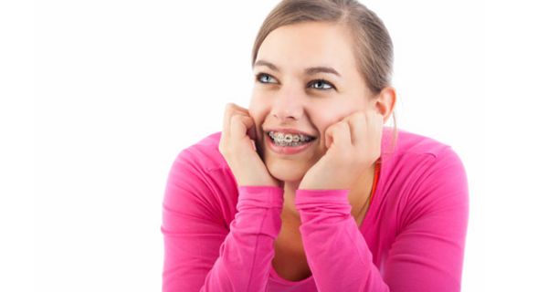 Junge Frau im knallrosa Pulli, aufgestützte Ellenbogen, zurückgebundene Haare lächelt breit, so dass man ihre Brackets sieht