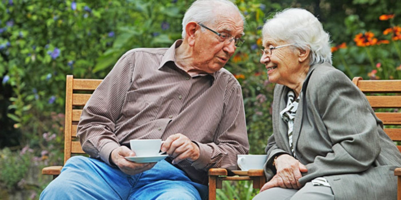 Altes Ehepaar im Garten auf einer Bank, sich froh anlachend