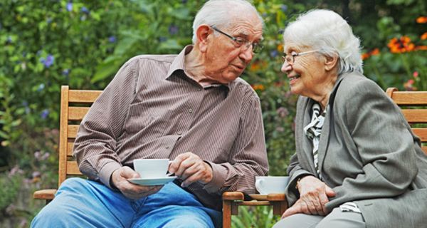 Altes Ehepaar im Garten auf einer Bank, sich froh anlachend