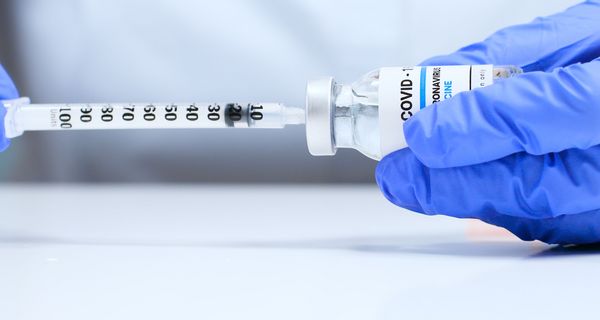 Arzt zieht mit einer Spritze eine Impfdosis aus einer Ampulle auf