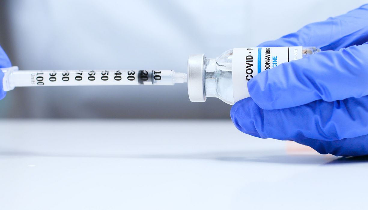 Arzt zieht mit einer Spritze eine Impfdosis aus einer Ampulle auf