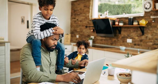 Mann, sitzt im Home Office am Laptop und wird von seinen zwei Kindern gestört.