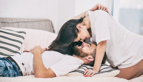 Mann, liegt im Bett, Frau beugt sich über ihn, beide lächeln.