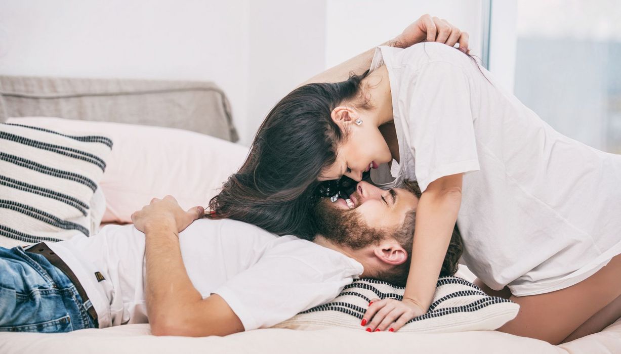 Mann, liegt im Bett, Frau beugt sich über ihn, beide lächeln.