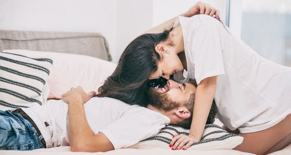 Mann, liegt im Bett, Frau beugt sich über ihn, beide lächeln.