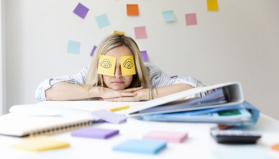 Junge Frau, liegt erschöpft auf ihrem Schreibtisch.