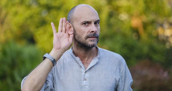 Mann, hält eine Hand an sein Ohr.