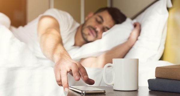 Mann, liegt im Bett und drückt auf sein Handy.