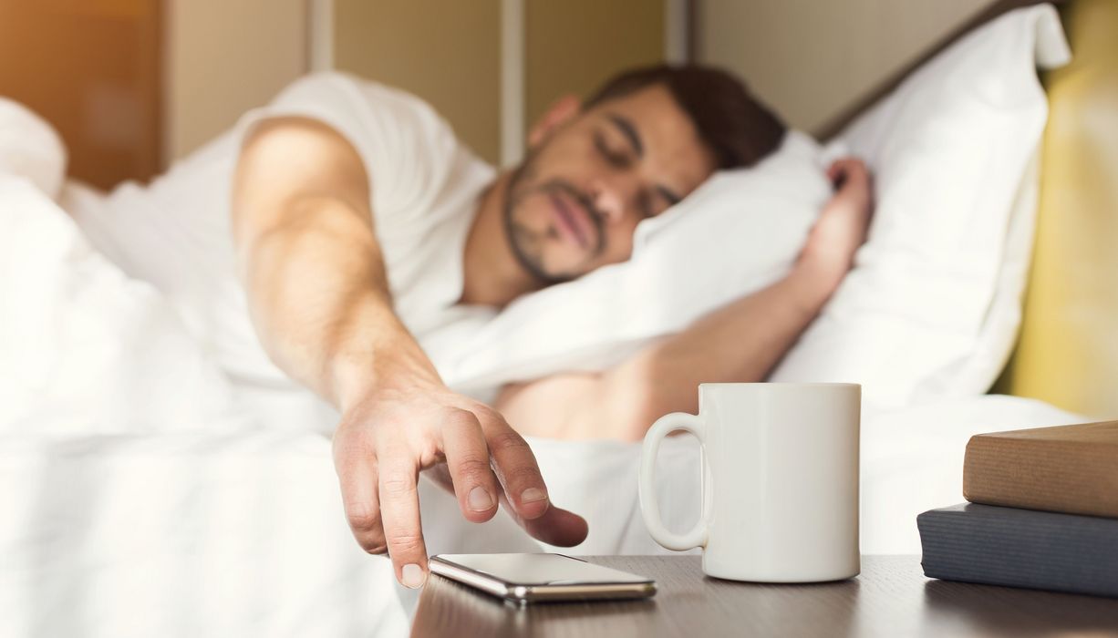 Mann, liegt im Bett und drückt auf sein Handy.