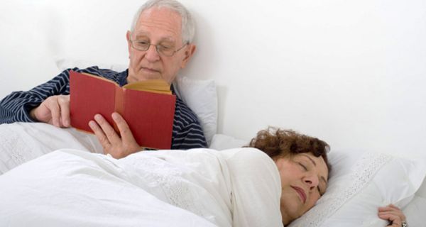 Paar im Bett, Mann (ca. 70) liest, Frau (ca. 60er) schläft