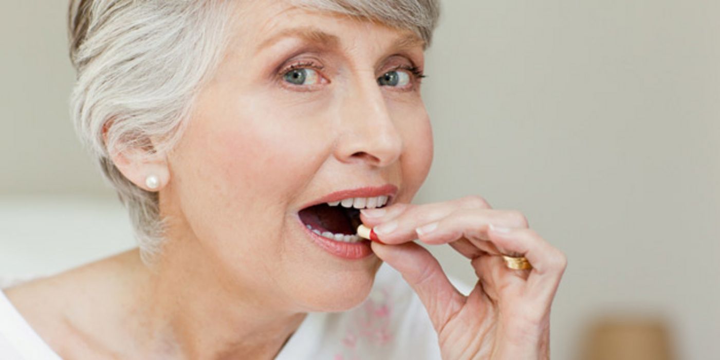 Ältere Frau mit grauer Kurzhaarfrisur bei der Tabletteneinnahme