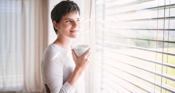 Kaffeetrinkende Frau blickt durch Fenster.