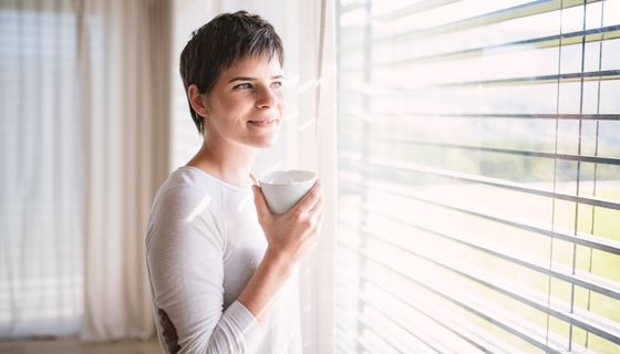 Kaffeetrinkende Frau blickt durch Fenster.