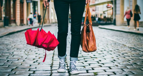 Frau in einer Stadt, mit einer Handtasche und einem Regenschirm in der Hand.