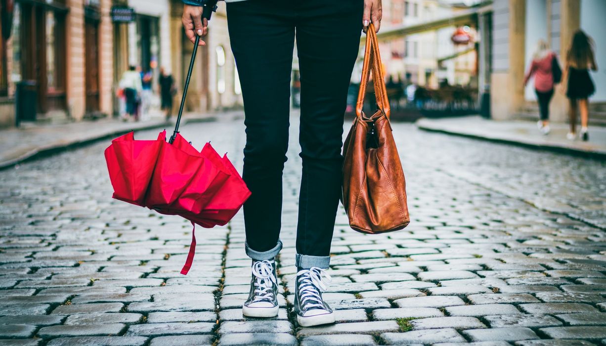 Frau in einer Stadt, mit einer Handtasche und einem Regenschirm in der Hand.