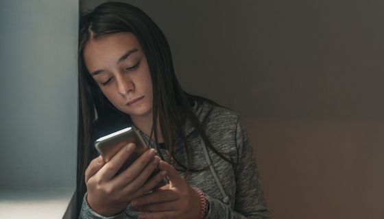 Junges Mädchen, schaut traurig auf ihr Smartphone.