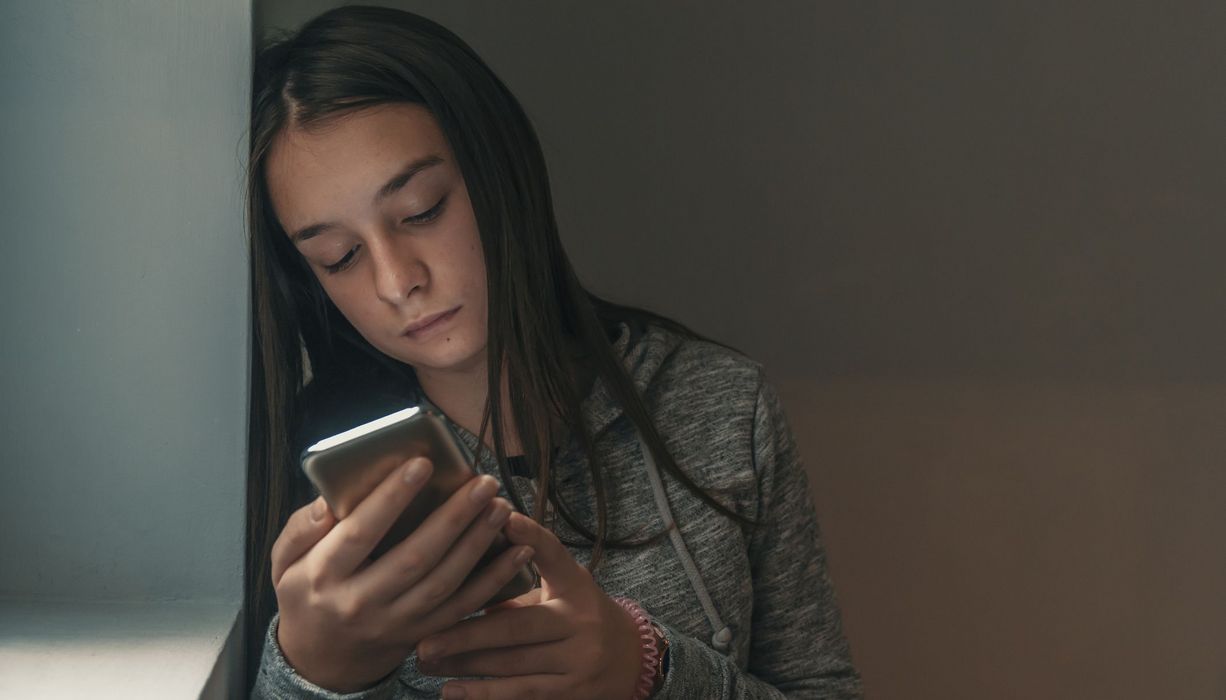 Junges Mädchen, schaut traurig auf ihr Smartphone.
