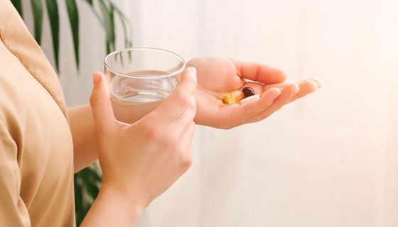 Frau, hält ein Glas Wasser und Tabletten in den Händen. 