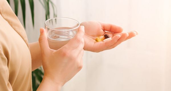 Frau, hält ein Glas Wasser und Tabletten in den Händen. 