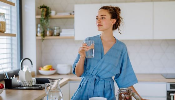 Junge Frau, steht mit einem Glas Wasser in der Küche.