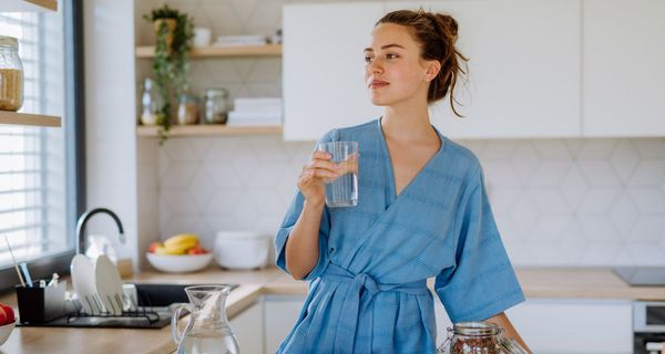 Junge Frau, steht mit einem Glas Wasser in der Küche.