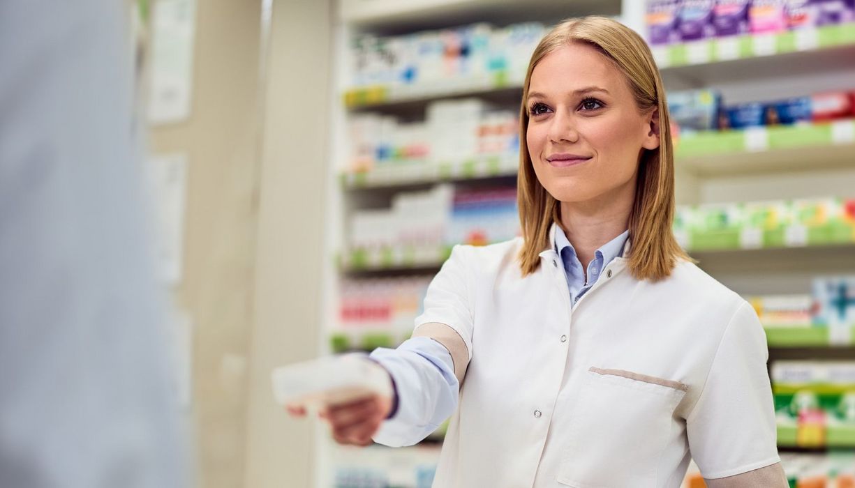 Eine junge Apothekerin reicht einem Kunden ein Medikament. 