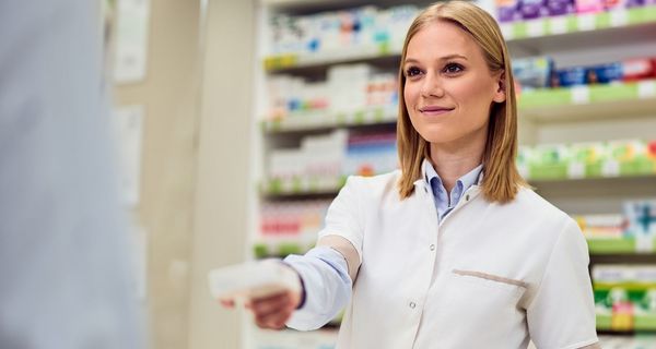 Eine junge Apothekerin reicht einem Kunden ein Medikament. 