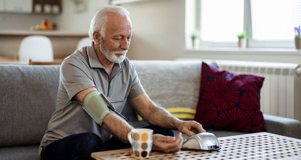 Älterer Mann, bedient ein Blutdruckmessgerät.