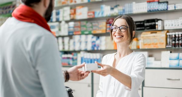 Apothekerin händigt Kunden ein Medikament aus.