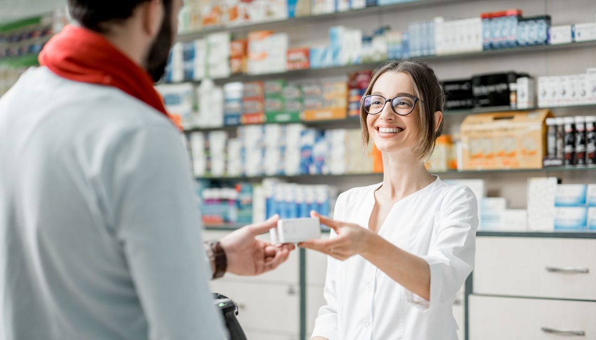 Apothekerin händigt Kunden ein Medikament aus.