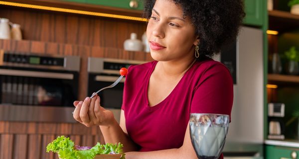 Frau blickt nachdenklich in die Ferne, während sie einen Salat isst. 