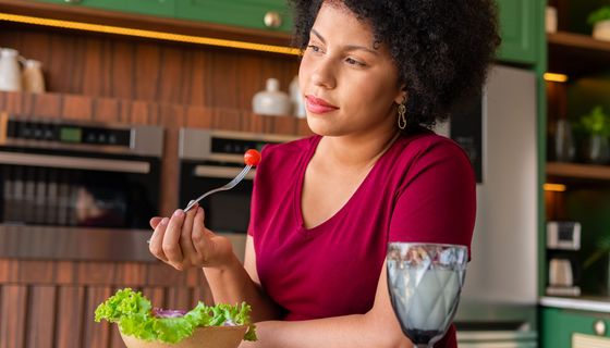 Frau blickt nachdenklich in die Ferne, während sie einen Salat isst. 