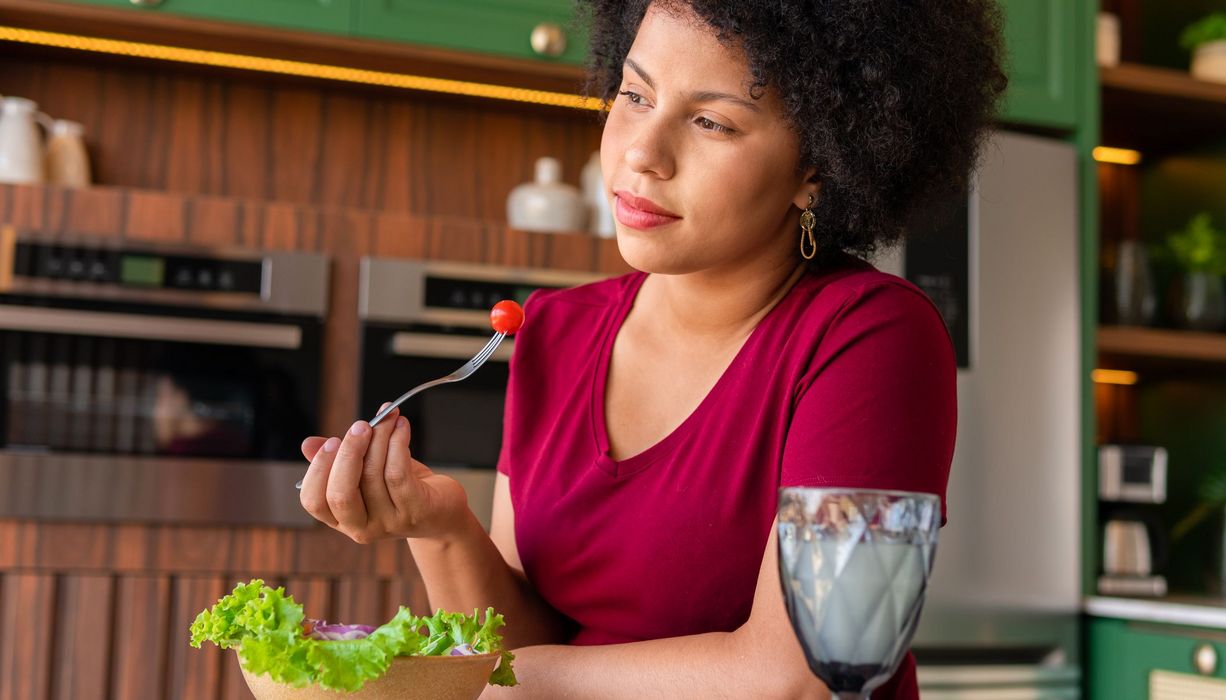 Frau blickt nachdenklich in die Ferne, während sie einen Salat isst. 