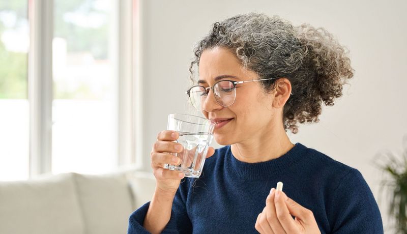 Frau über 40 nimmt eine Tablette mit einem Glas Wasser ein.