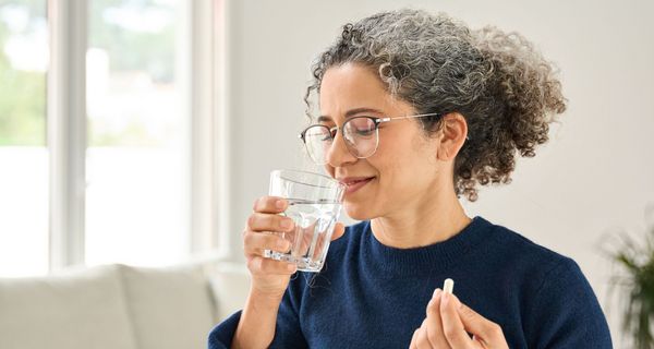 Frau über 40 nimmt eine Tablette mit einem Glas Wasser ein.
