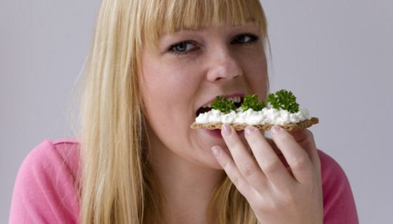 Junge blonde Frau beißt in ein Knäckebrot mit Frischkäse und frischen Kräutern
