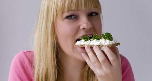 Junge blonde Frau beißt in ein Knäckebrot mit Frischkäse und frischen Kräutern