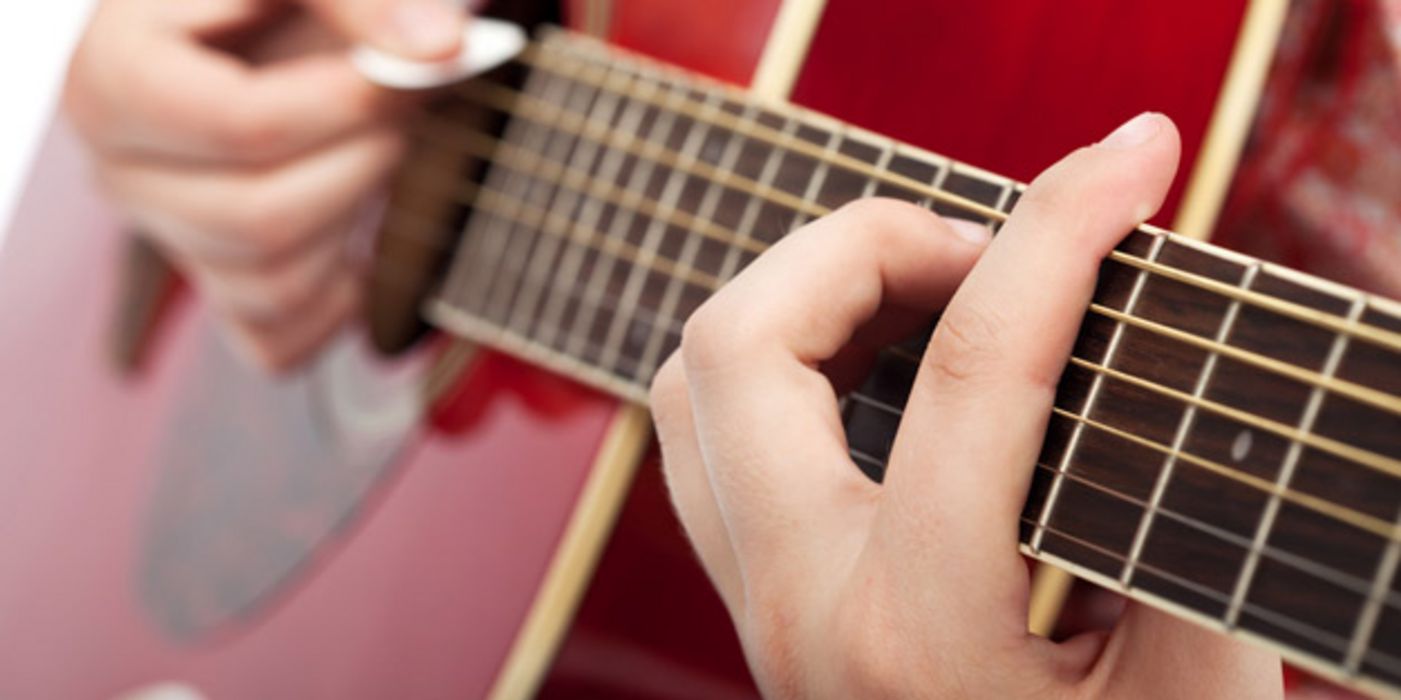 Hände beim Spielen auf rotlackierter Akustikgitarre