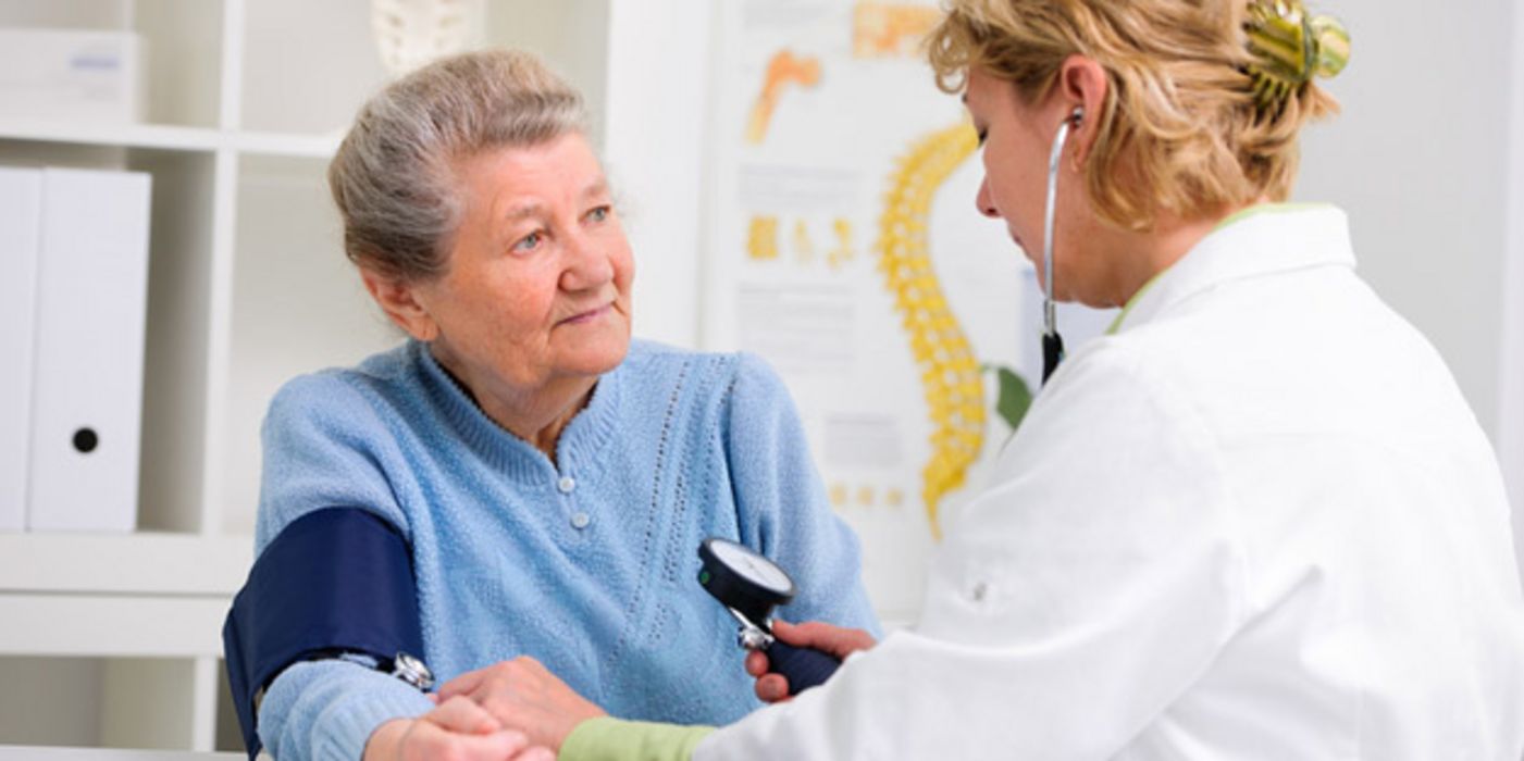 Seniorin (70+) in hellblauem Pulli bekommt von Ärztin in Praxis den Blutdruck gemessen