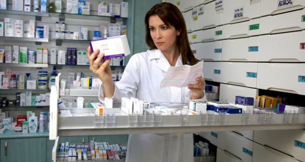 Apothekerin an ausgezogener Medikamentenschublade schaut prüfend auf Medi-Schachtel in der Hand