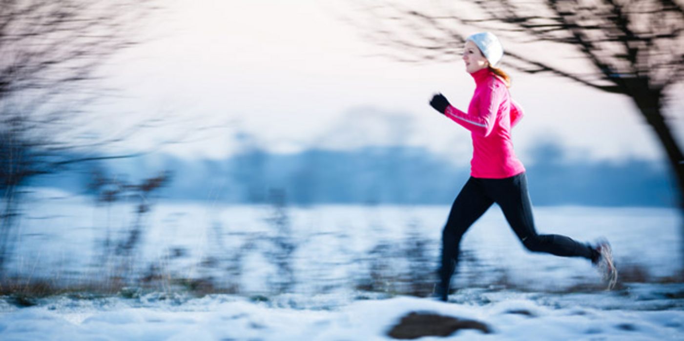 Frau beim Joggen im Schnee, Wald, Bäume, Lichtung, zyklamfarbenes Oberteil, schwarze Hose, Mütze, rechter Bildrand
