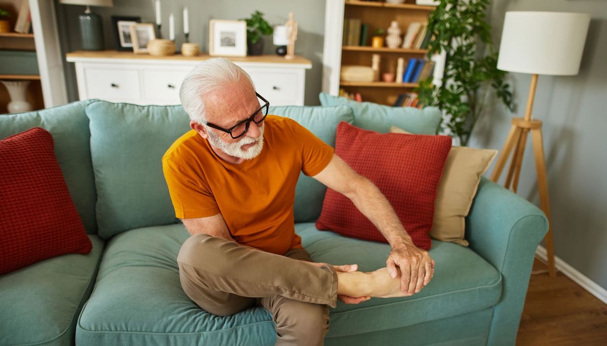 Älterer Mann sitz auf dem Sofa und betrachtet seinen Fuß.