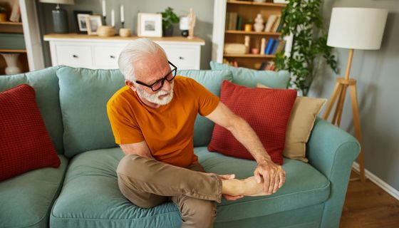 Älterer Mann sitz auf dem Sofa und betrachtet seinen Fuß.