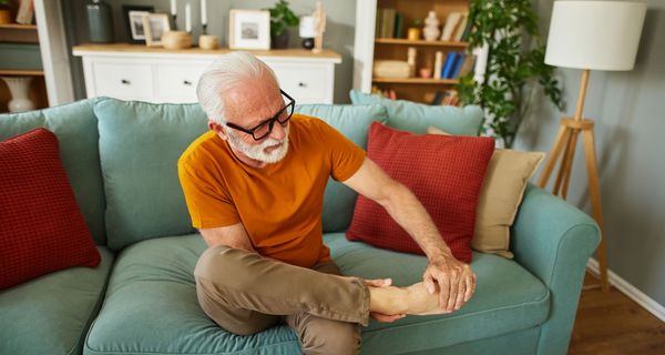 Älterer Mann sitz auf dem Sofa und betrachtet seinen Fuß.