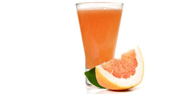 Glas Grapefruitsaft mit aufgeschnittener Frucht daneben