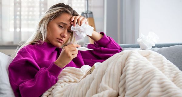 Frau liegt krank auf dem Sofa und misst Fieber
