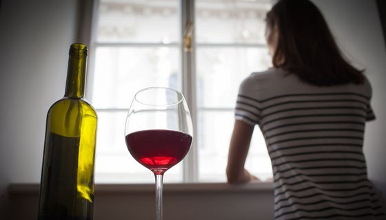 Frau steht am Fenster, hinter ihr stehen eine Weinflasche und Glas mit Rotwein